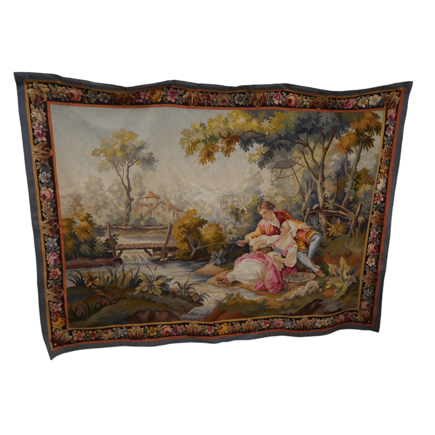 A 20th Aubusson wall hanging of a young man and lady fishing in a river in the foreground with a wooden bridge, house and chateau in the background, 169 cm wide, 122 cm high. Condition - good